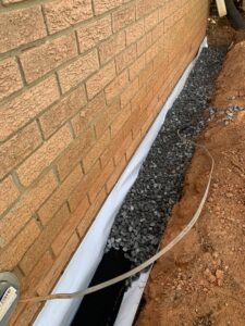 An exterior French drain being installed next to a brick foundation by Wetlock Waterproofing in Rock Hill, SC.