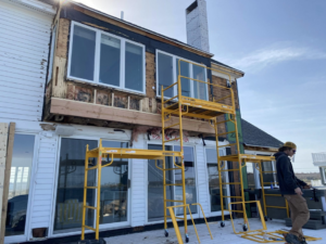 Exterior of a house with siding removed for water damage repair, showing scaffolding by Rival Property Maintenance in Biddeford, ME.