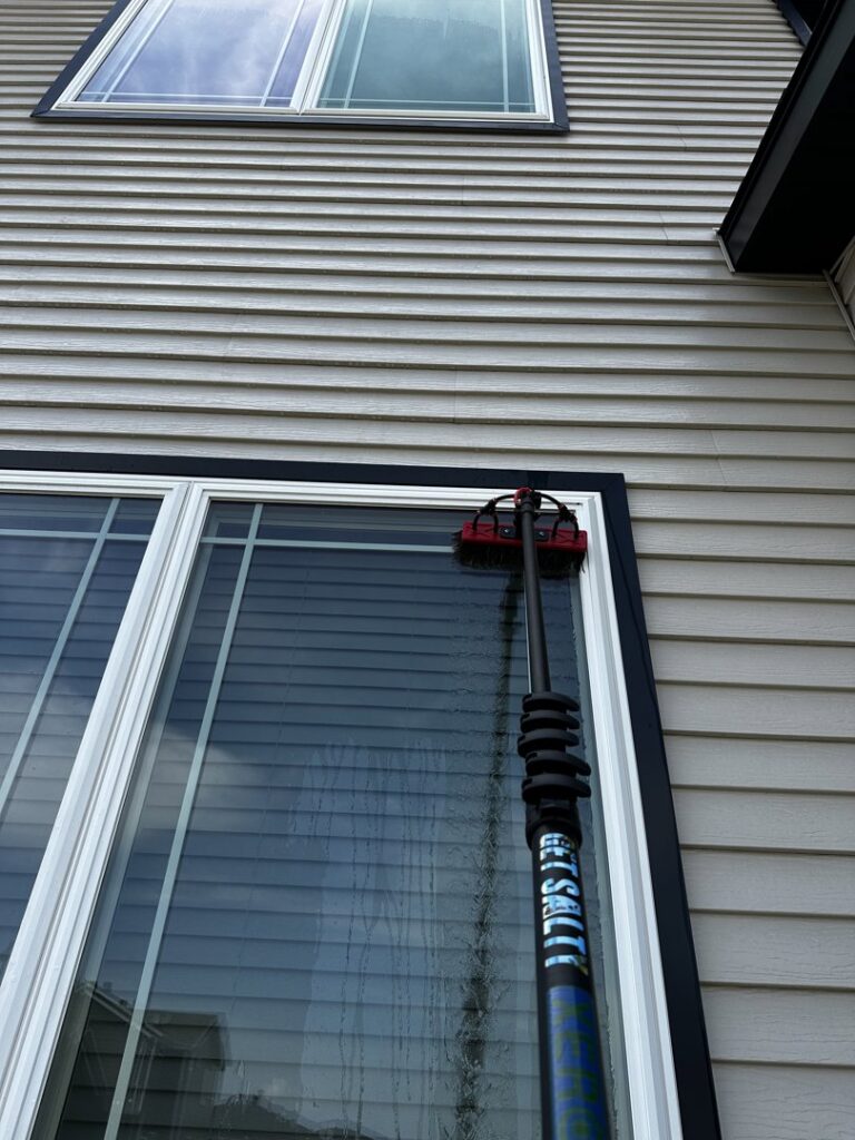 A long-handled brush being used for exterior window cleaning on a house by FM Cleaning in West Fargo, ND.
