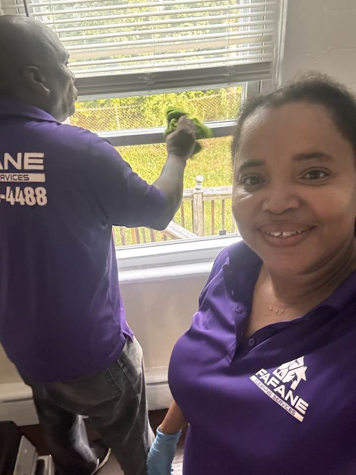A Fafane Cleaning Services team member expertly cleaning a window while another smiles, providing house cleaning in Boston, MA.