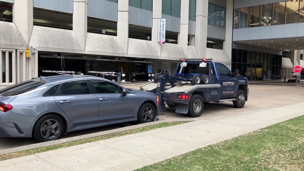 A Fast Tow wrecker truck actively towing a grey sedan on a city street in Houston, TX.