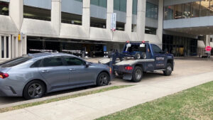 A Fast Tow wrecker truck actively towing a grey sedan on a city street in Houston, TX.
