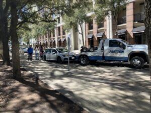 A Fast Tow wrecker truck actively towing a silver car on a tree-lined street in Houston, TX.
