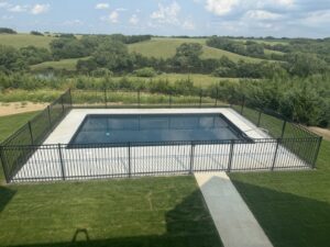 A completed rectangular swimming pool enclosed by a black fence with a concrete path, installed by Acapulco Pool and Spa LLC in Los Angeles, CA