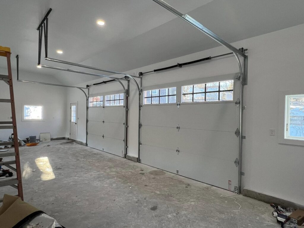 A finished garage interior featuring two white garage doors and openers installed by NDI Garage Door in Plaistow, NH.