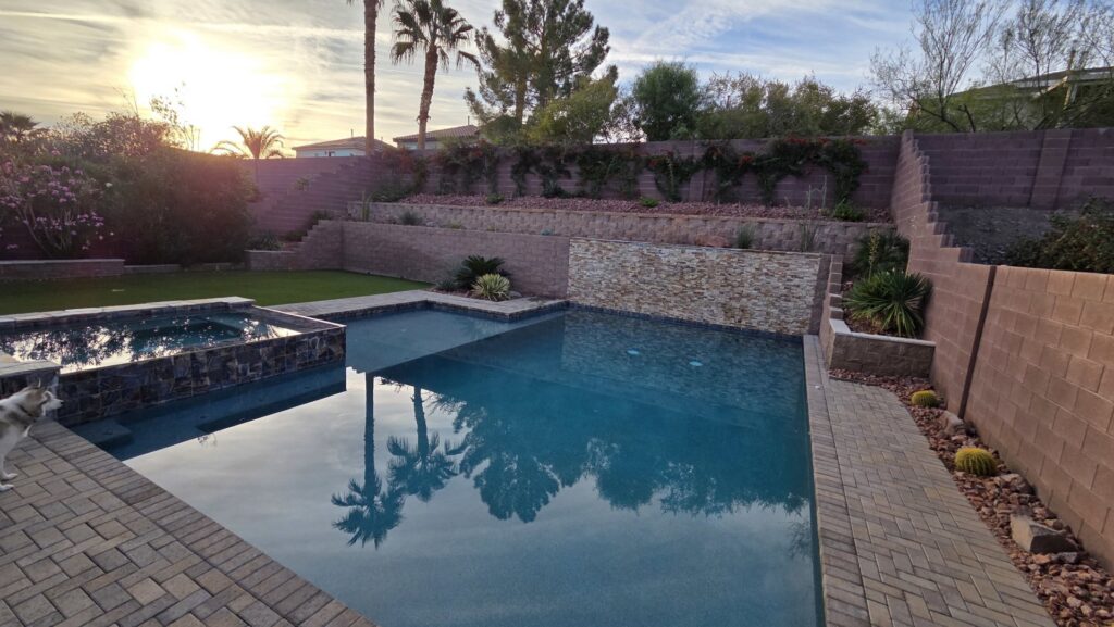 A beautifully finished pool and spa surrounded by pavers and landscaping at sunset by Fix A Pool in Las Vegas, NV