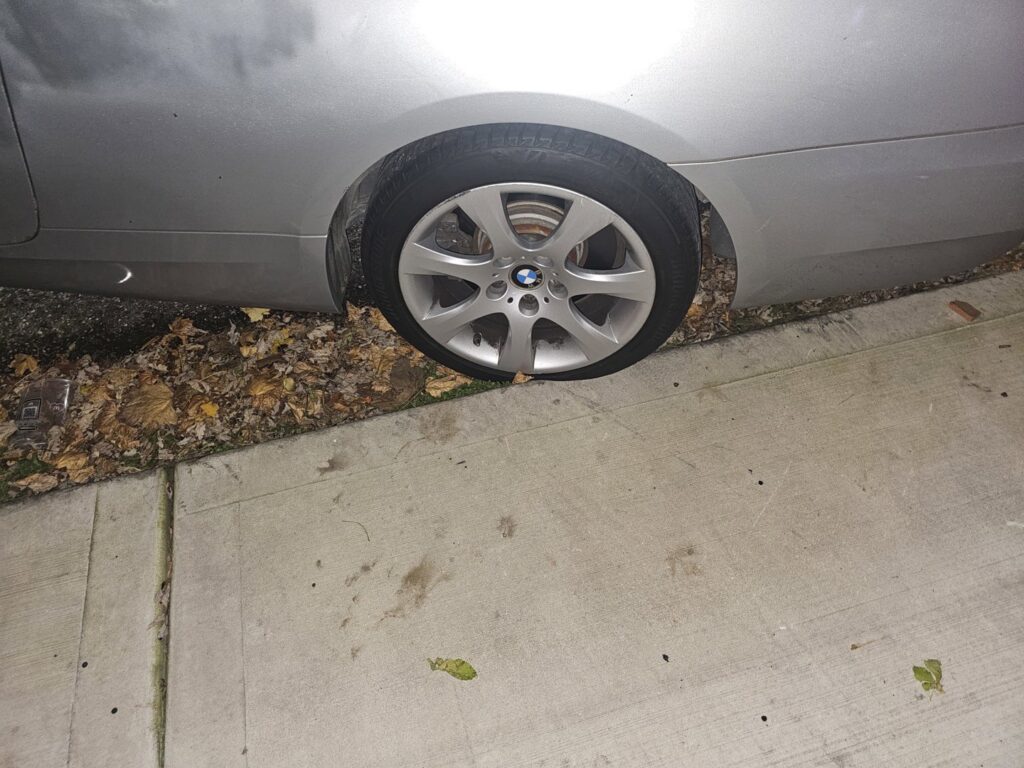 A silver BMW with a flat tire on a sidewalk, indicating a need for roadside assistance or towing from Bino's Towing in Chicago, IL.