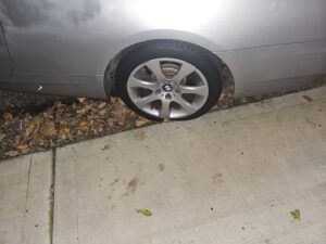 A silver BMW with a flat tire on a sidewalk, indicating a need for roadside assistance or towing from Bino's Towing in Chicago, IL.