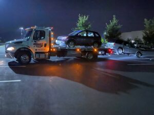 A white flatbed tow truck from Hank's Auto Service performing a double tow of two SUVs at night in Bethlehem, PA.