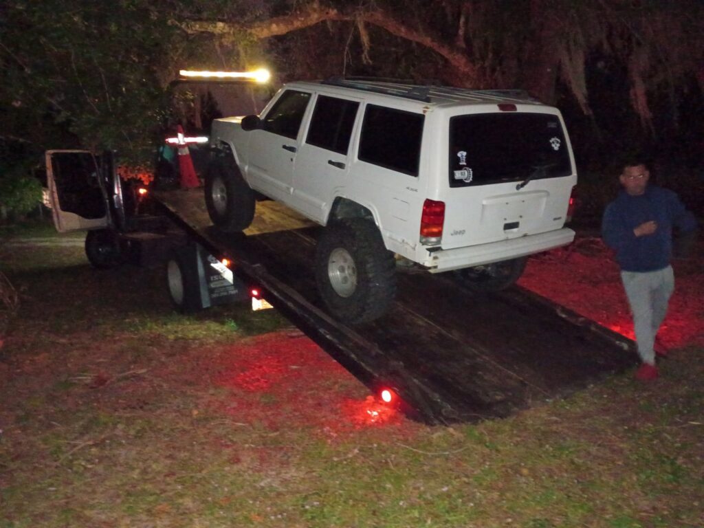 A white flatbed tow truck from Always Ready Towing loading a white Jeep Cherokee at night in North Fort Myers, FL.