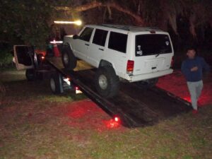A white flatbed tow truck from Always Ready Towing loading a white Jeep Cherokee at night in North Fort Myers, FL.