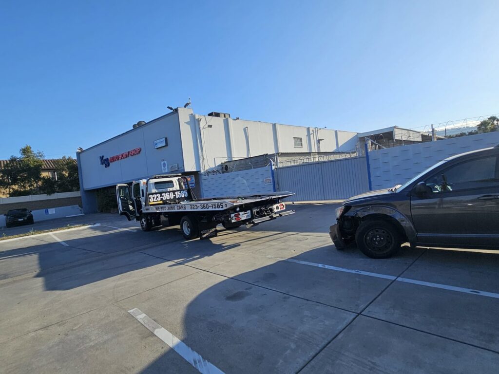 Orellanas Towing & Junk Car flatbed tow truck preparing to tow a damaged dark grey car in Los Angeles, CA.