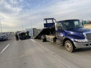 A flatbed tow truck from Automotive Technical Services at the scene of an overturned trailer on a highway in Boise, ID.