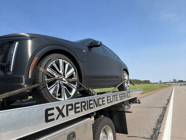 An Elite Towing of Minnesota flatbed tow truck transporting a dark grey car on a highway in St Paul, MN.