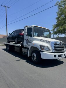 A flatbed tow truck from Leos Towing Service carrying a black SUV in Anaheim, CA.