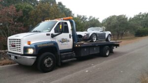 A flatbed tow truck from Alanis Wrecker Service carrying a grey sports car in San Antonio, TX.
