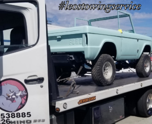 A flatbed tow truck from Leos Towing Service carrying a vintage light blue Ford Bronco body in Anaheim, CA.