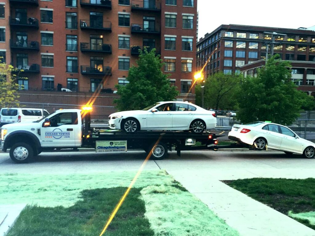 A flatbed tow truck from Chicago Towing double towing two white sedans in Chicago, IL.