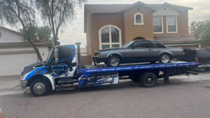 A flatbed tow truck from CnD towing carrying a grey car in Phoenix, AZ.