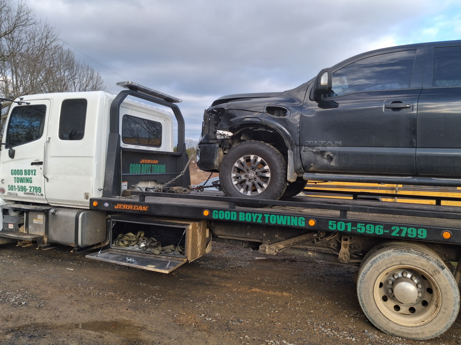 A flatbed tow truck from National Tow List hauling a damaged black pickup truck in Cove, AR.