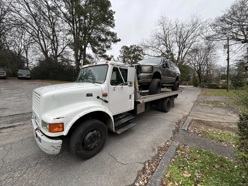 A white flatbed tow truck from Jb's Towing & Recovery hauling a dark SUV in Rossville, GA.