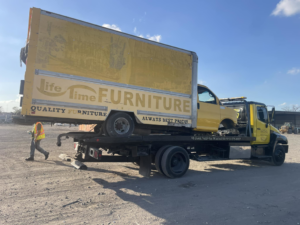 A yellow flatbed tow truck from Houston Towing loading a yellow box truck onto its bed in Houston, TX.