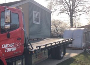 A red flatbed tow truck from Chicago Towing preparing to load a large, white, rounded object in Chicago, IL.