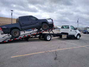 A flatbed tow truck from Primo Towing loading a dark pickup truck in Anderson, IN.