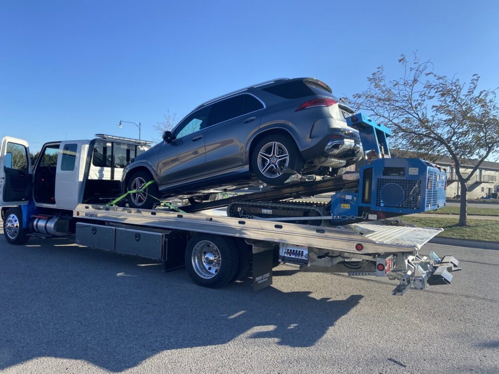 A flatbed tow truck from Jim & Ron's Service Inc. loading a grey SUV in Sioux Falls, SD.