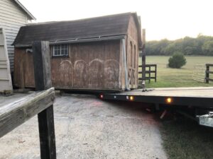 A red flatbed tow truck from Rubber Chicken Towing LLC loading a wooden shed onto its bed in Charlotte, NC.