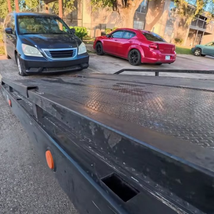 A flatbed tow truck with a dark blue minivan and red sedan in a parking lot, ready for towing by Fort Benning Towing in Columbus, GA