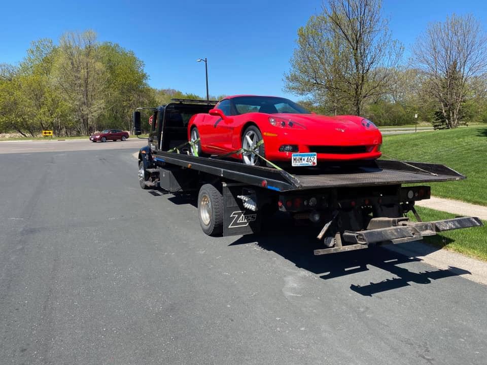 An Elite Towing of Minnesota flatbed tow truck transporting a red Corvette on its bed in St Paul, MN.