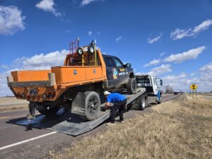 A flatbed tow truck from Jim & Ron's Service Inc. securing a pickup truck on its bed in Sioux Falls, SD.