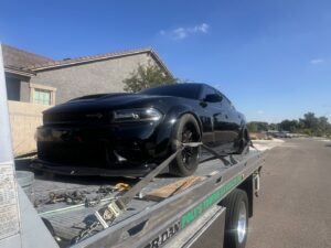 A flatbed tow truck from Poly's Towing Glendale, AZ, transporting a black Dodge Charger.