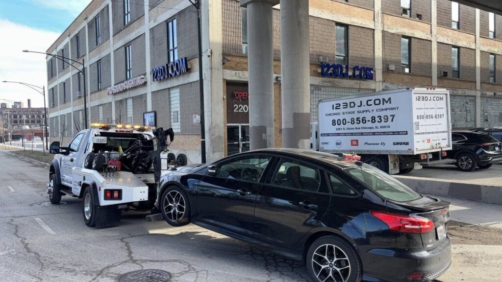 A flatbed tow truck from Chicago Towing towing a black sedan with a wheel lift in Chicago, IL.