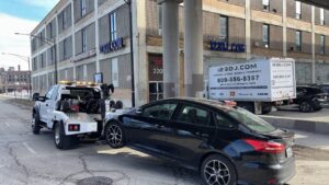 A flatbed tow truck from Chicago Towing towing a black sedan with a wheel lift in Chicago, IL.
