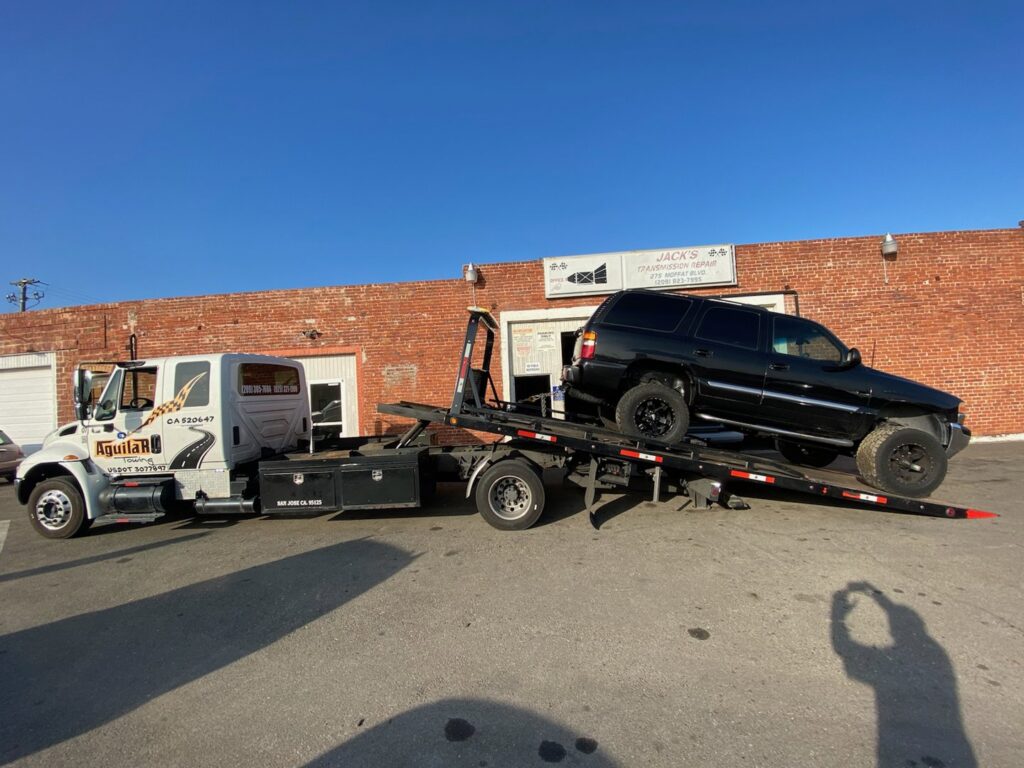 Aguilar Towing's flatbed tow truck transporting a black SUV to Jack's Transmission Repair in San Jose, CA