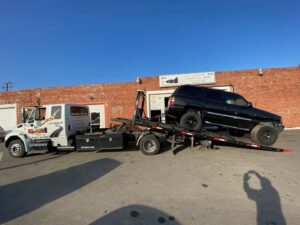 Aguilar Towing's flatbed tow truck transporting a black SUV to Jack's Transmission Repair in San Jose, CA