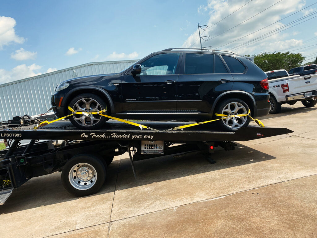 A flatbed tow truck from Rosco's Towing Services LLC towing a black SUV secured with yellow straps in Carencro, LA.