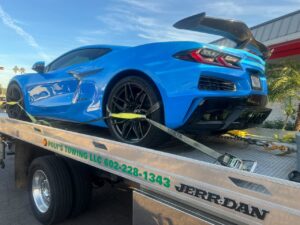 A flatbed tow truck from Poly's Towing Glendale, AZ, transporting a blue Corvette sports car.