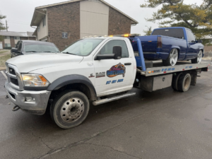 A white flatbed tow truck from Danny's Towing Edgar towing a blue pickup truck in Indianapolis, IN.
