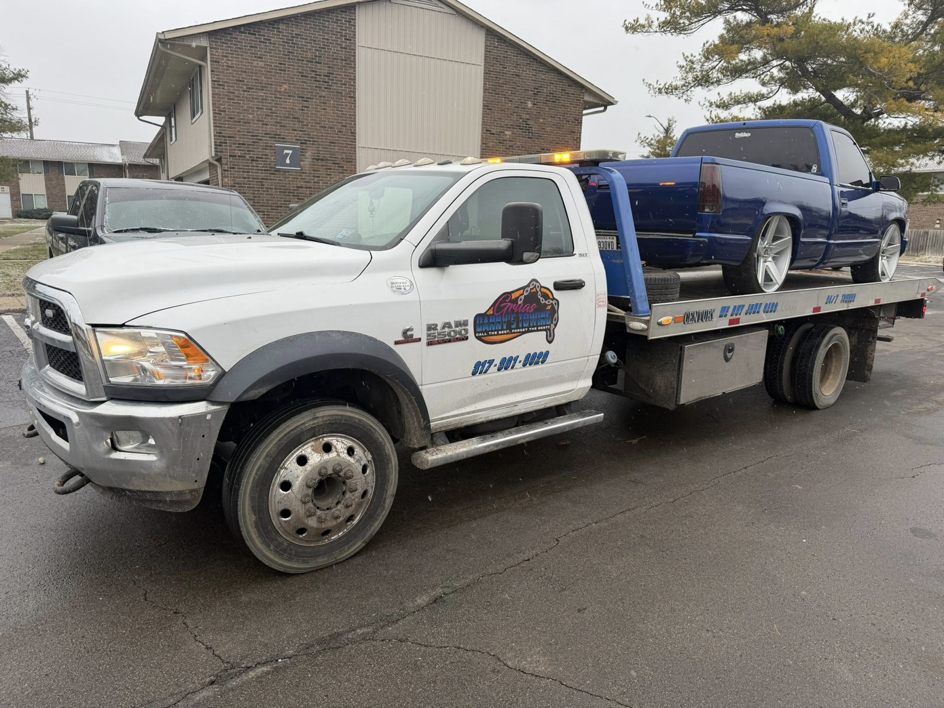 A white flatbed tow truck from Danny's Towing Edgar towing a blue pickup truck in Indianapolis, IN.