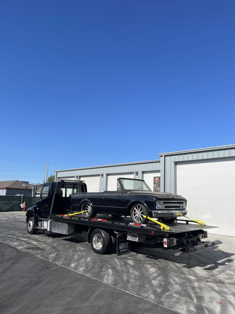 A black flatbed tow truck from A&R towing LLC transporting a classic black convertible car in Nampa, ID.