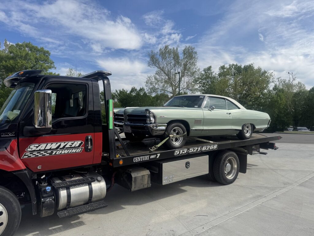 A classic light green car is securely loaded on a flatbed tow truck from Sawyer Towing in Cincinnati, OH.