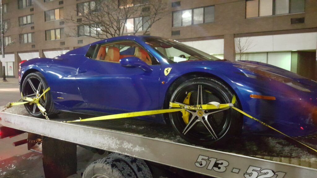 A blue Ferrari sports car is securely loaded on a flatbed tow truck from Sawyer Towing in Cincinnati, OH.