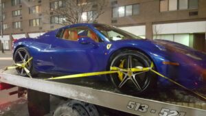 A blue Ferrari sports car is securely loaded on a flatbed tow truck from Sawyer Towing in Cincinnati, OH.