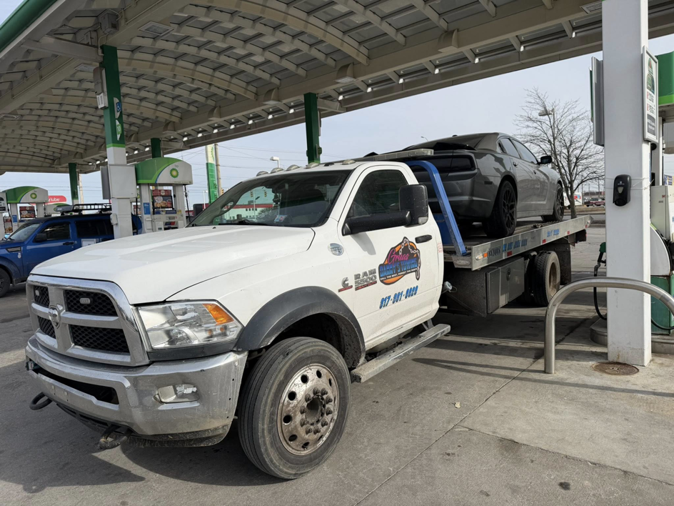A white flatbed tow truck from Danny's Towing Edgar towing a grey car at a gas station in Indianapolis, IN.