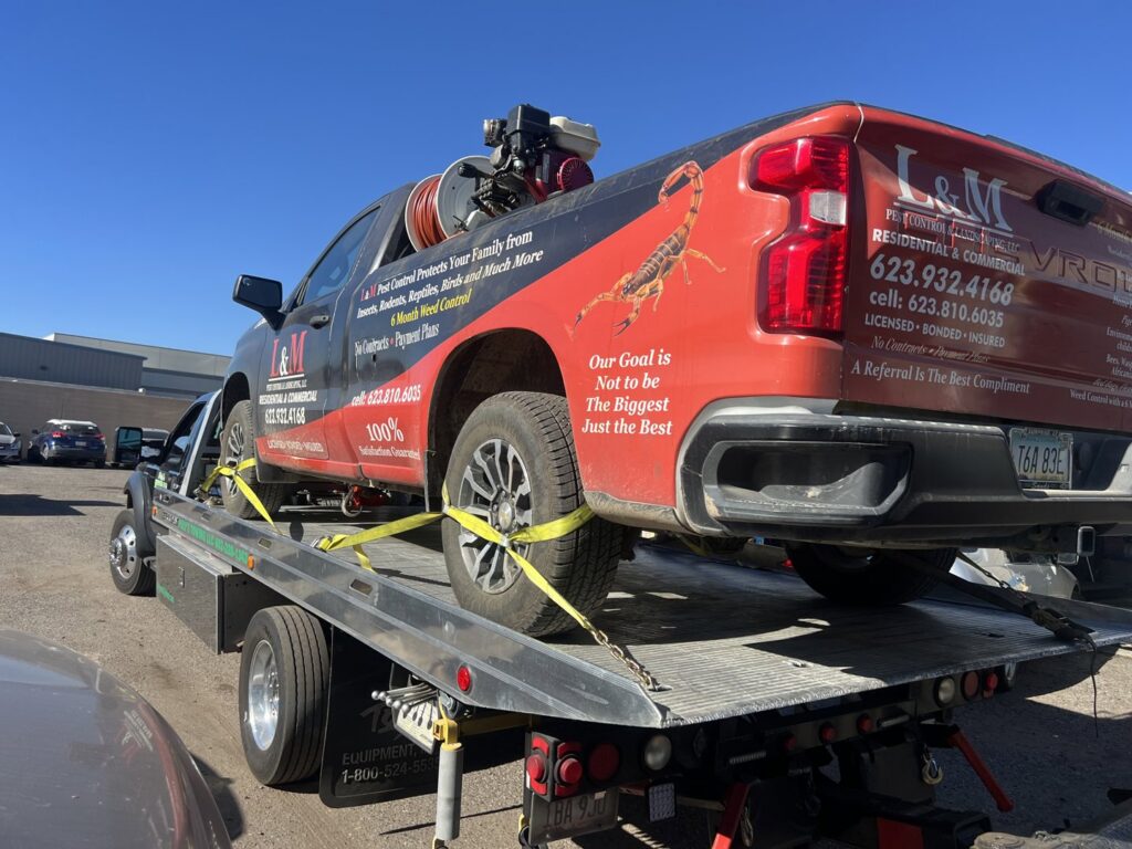 A flatbed tow truck from Poly's Towing Glendale, AZ, transporting a red pest control pickup truck.