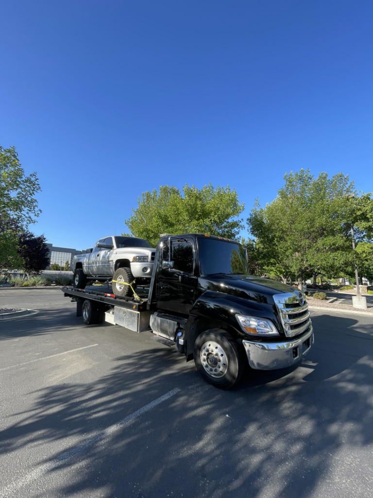 A black flatbed tow truck from A&R towing LLC transporting a white pickup truck in Nampa, ID.
