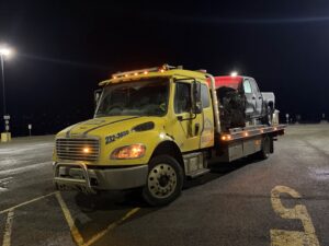 A Help Line Towing flatbed truck transporting a pickup truck at night in Wasilla, AK.